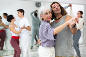 Happy caucasian guy and old lady practising paired latin dance in dance studio