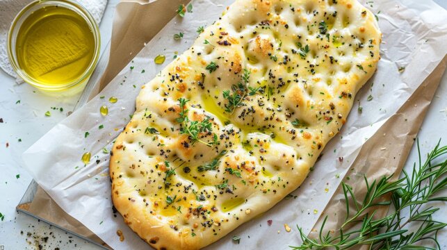 Top view of flatbread topped with herbs and olive oil on a parchment paper.
