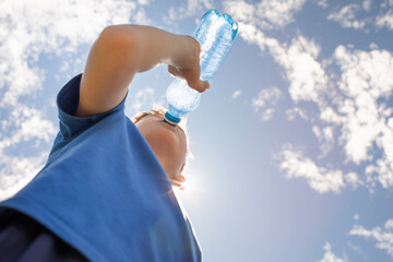 little boy drinking water from bottle on a hot summer day, thirsty child drinks from water bottle replenish fluids in summer heat wave 
