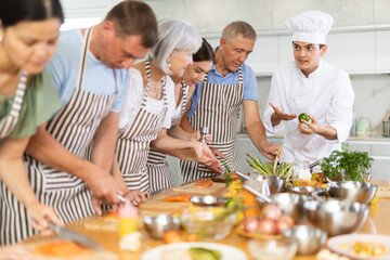 Earnest young male instructor of culinary classes explaining his students how to prepare salmon for...