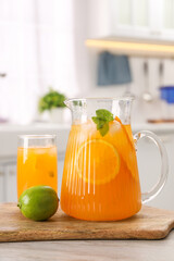 Tasty lemonade with orange in jug, glass and lime on wooden table in kitchen
