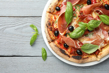 Tasty pizza with cured ham, olives, sun-dried tomato and basil on gray wooden table, top view. Space for text