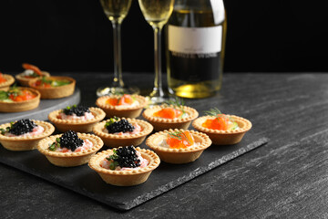 Delicious canapes with salmon and caviar on black textured table, closeup
