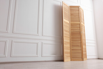 Folding screen near white wall indoors, low angle view. Space for text