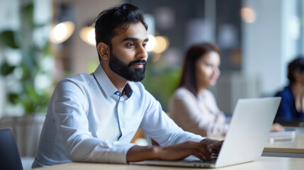Focused Indian professional using a laptop to share insights during a business meeting with coworkers