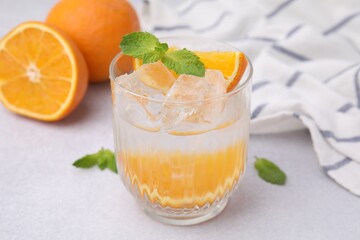 Refreshing water with orange and mint in glass on light table, closeup