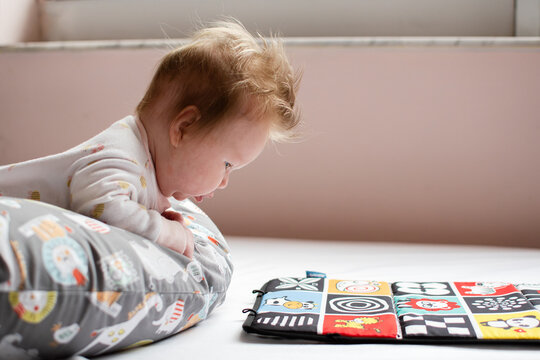 Little cute Caucasian baby girl doing tummy time. Tummy time for newborns on nursing pillow. High-contrast learning cards for babies - Powered by Adobe
