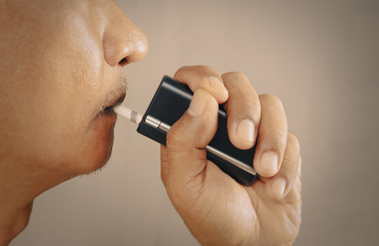 Side image of old asian man is using the Heat not burn type(HNB) Electronic cigarette heater, It's hybrid cigarette smoking device