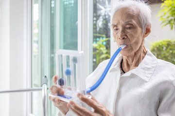 Asian senior patient exercising her lungs,using incentive spirometer,measuring the air capacity of...