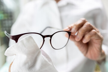 Hands of senior woman holding eyeglasses,elderly cleaning the lenses of glasses with her shirt,old...