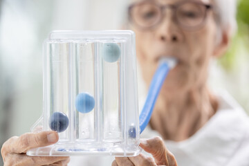 Asian senior woman using incentive spirometer,tool to help the lung expansion,exercise the lung,old...