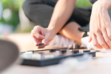 Close up of Asian teenage boy hand and girl playing board game, Asian brother and sister relaxing hobbies playing a game of checkers outdoor