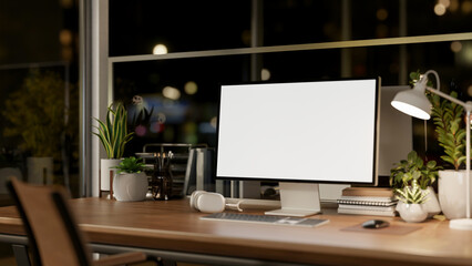 A computer mockup on a wooden table in a modern office at night, illuminated by a table lamp.