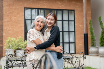 A happy mature Asian grandma is hugging her lovely granddaughter in a home garden on a bright day.