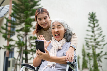 A happy Asian grandma in wheelchair and her granddaughter are enjoying a video call with a relative.