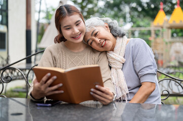 A positive Asian granddaughter and her lovely grandma are enjoying reading a book together outdoors.