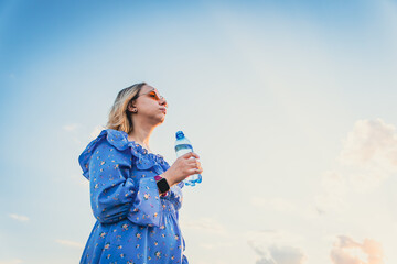 Young Woman Enjoys Refreshing Water While Standing Under a Beautiful Sunset in the Summer