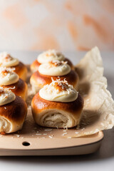 Close up Freshly baked buns topped with cream cheese and shredded coconut on a baking tray with parchment on side view