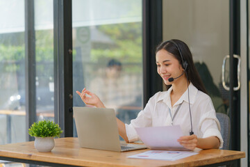 Happy smiling operator Asian woman customer service agent with headsets working on a computer in a call center.