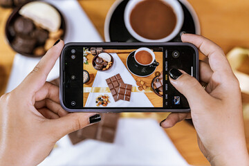 Woman with cell phone in her hand taking a picture of her chocolate business. International...