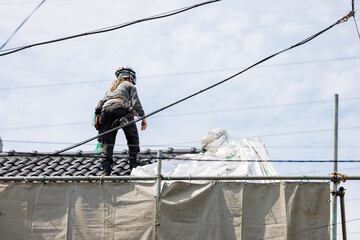 住宅の解体のために屋根の上で作業をする作業員