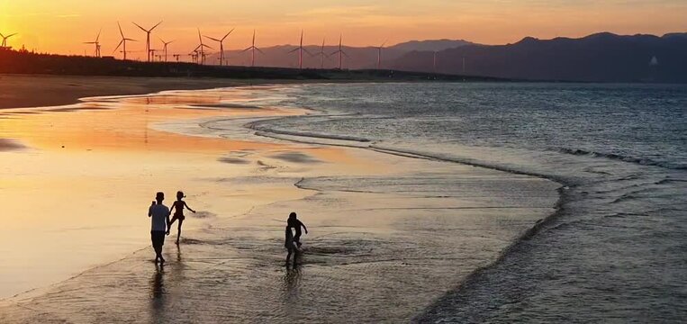Sunset over the beach in Quy Nhon, Binh Dinh, Vietnam.Silhouettes of a father and his three children walking along the beach, heartwarming scene .Wind turbines, renewable energy at serene seascape