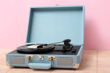 Record player with vinyl disk on table near pink wall