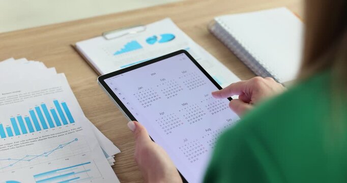 Woman manager flips through a calendar on tablet sitting at desk in office