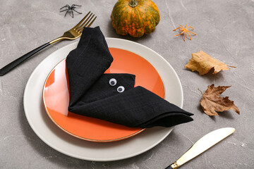 Festive table setting with napkin folded in shape of Halloween bat on grey grunge background