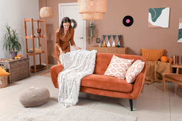 Young woman with warm plaid on sofa at home