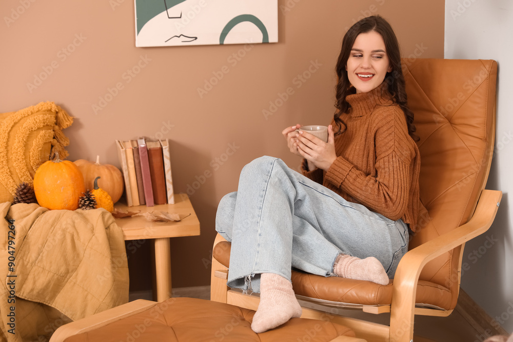 Canvas Prints Young woman with cup of hot coffee sitting in armchair at home on autumn day