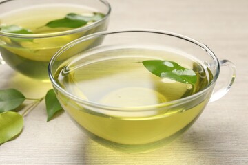 Refreshing green tea in cups and leaves on wooden table, closeup