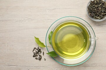 Refreshing green tea in cup and leaves on wooden table, flat lay. Space for text
