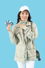 Stylish young Asian woman pointing at credit cards on blue background