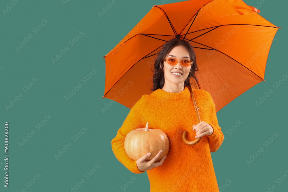 Canvas Prints Young Asian woman in fall clothes with umbrella and pumpkin on green background