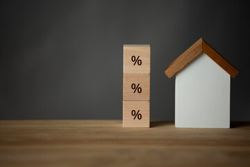 Wooden house with a stack of wooden block written with percentage on gray background with copy space.