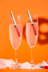Glasses of delicious cocktail with syringes for Halloween celebration on orange background
