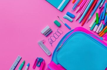 Back to school concept with colorful stationery and backpack on a pink background, laid flat. A top view of books, pens, pencils, markers and other school supplies in an open blue bag isolated on a pa