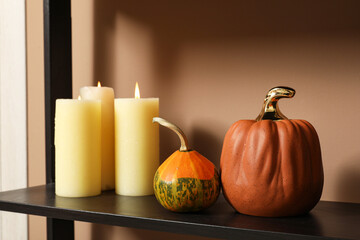 Halloween pumpkins with burning candles on shelf near beige wall, closeup