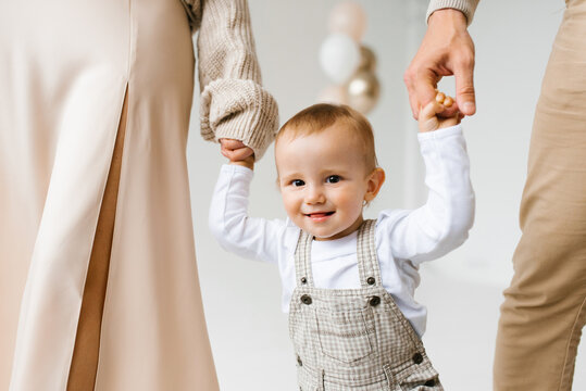 Happy one year old boy holding hands with mom and dad and smiling