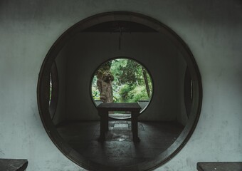 A circular doorway framed by white walls provides a glimpse of a lush, green garden with a pond and trees.