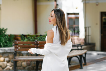 Happy woman in white casual clothes smiles while walking through the city streets in summer
