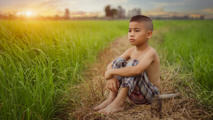 farmer boy asian sitting on a ridge alone in the grass-green countryside face looking emotionally depressed