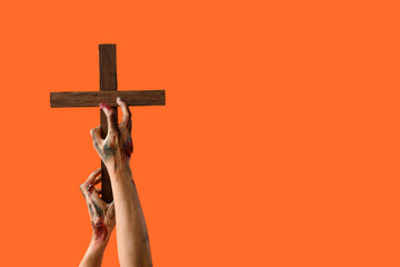 Zombie hands with wooden cross on orange background. Halloween celebration