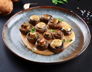 Baked champignons with herbs and spices in a ceramic plate on wooden background