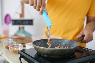 Man's Hand Frying Chicken Meat On Pan in The Kitchen