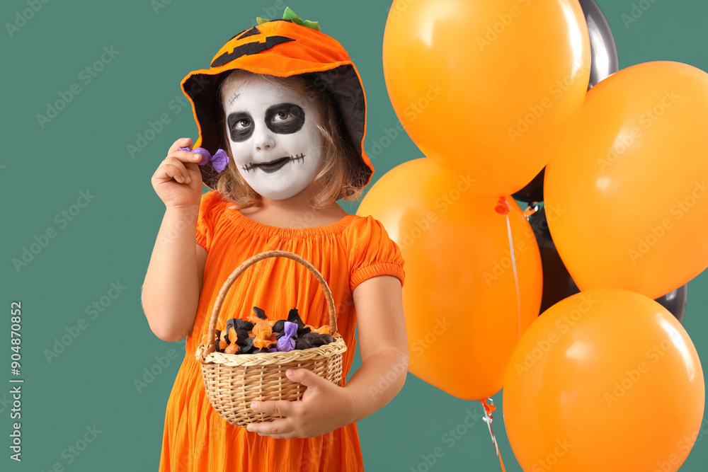 Wall mural little girl dressed for halloween with candies and balloons on green background