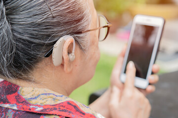 Mature woman with hearing aid using smartphone at outdoor.