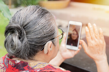 Senior woman with a hearing aid behind the ear communicates with her family via video