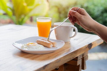 The woman eat by fork with breakfast on the table. American style breakfast with fried eggs, sausage, coffe and juice.